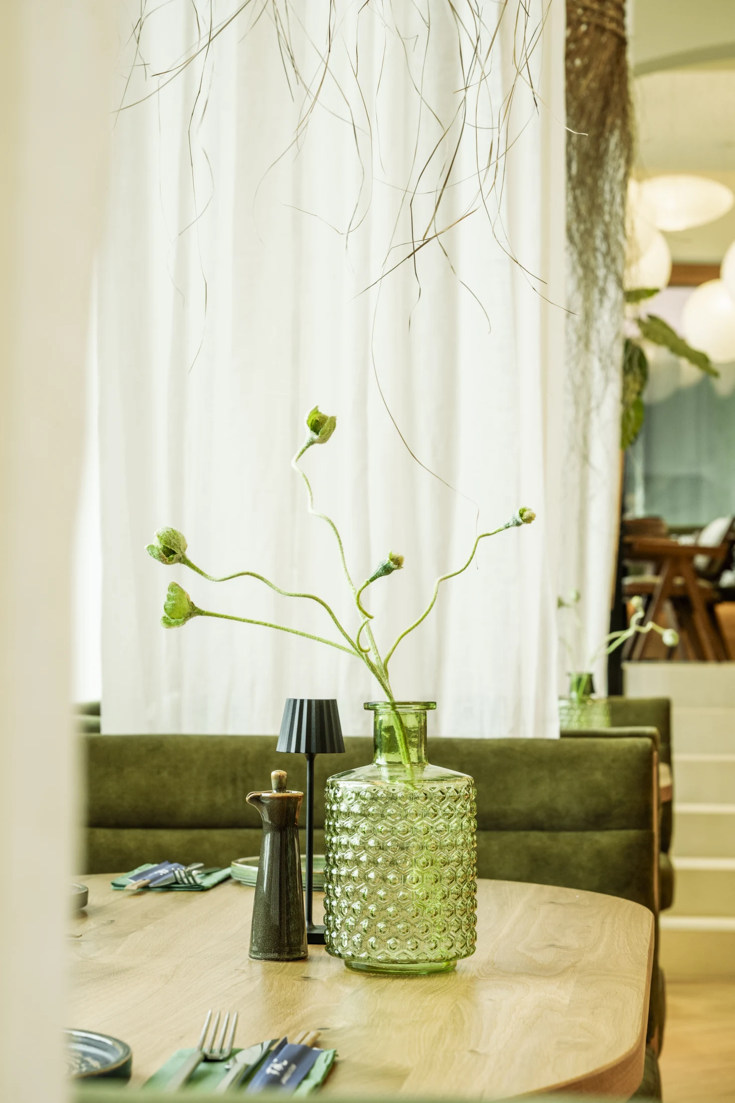 Tischdetail mit grüner Strukturglas-Vase, Blütenzweigen und Keramik-Sojakännchen
